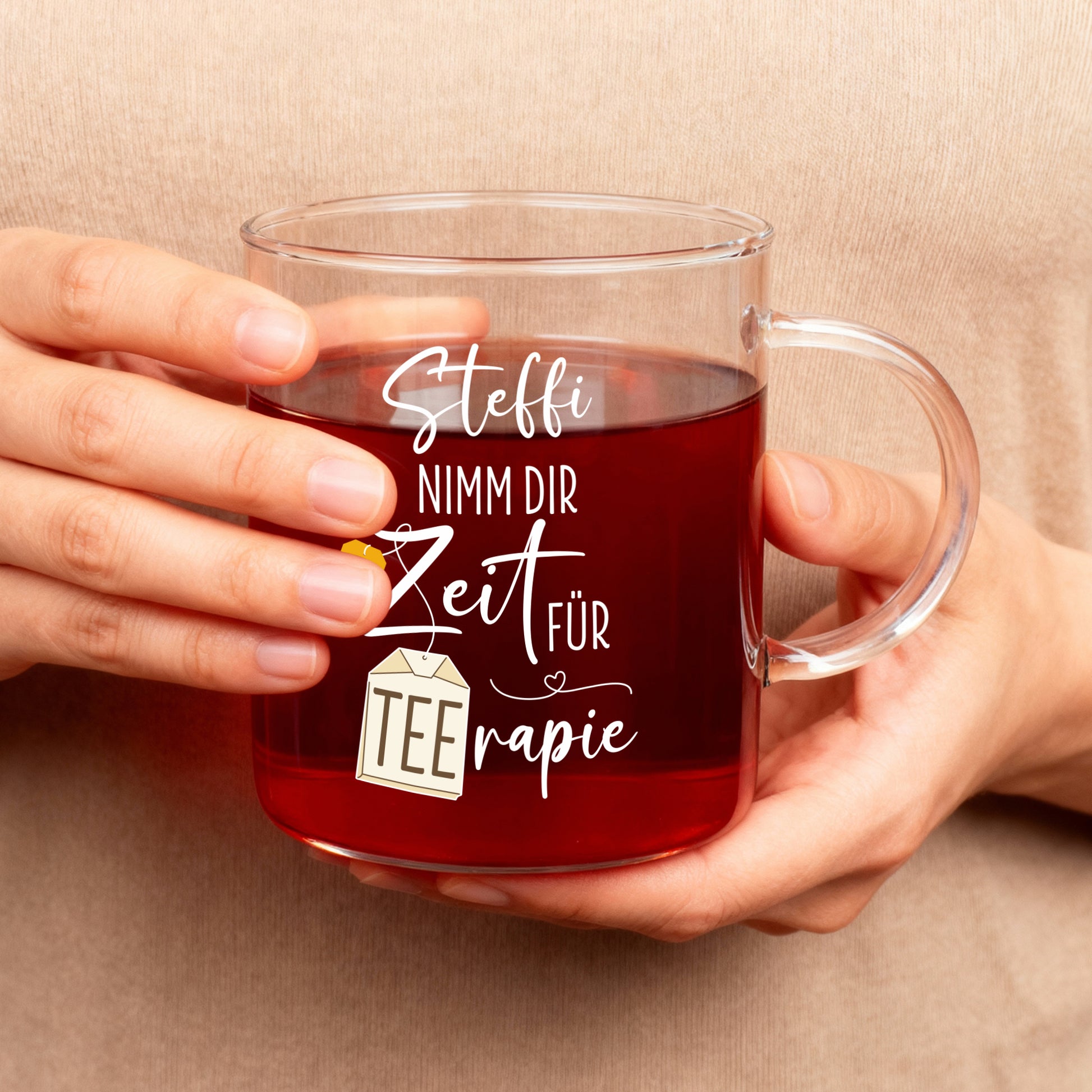 Teeglas mit personalisiertem TEErapie-Spruch und Name, in Händen gehalten