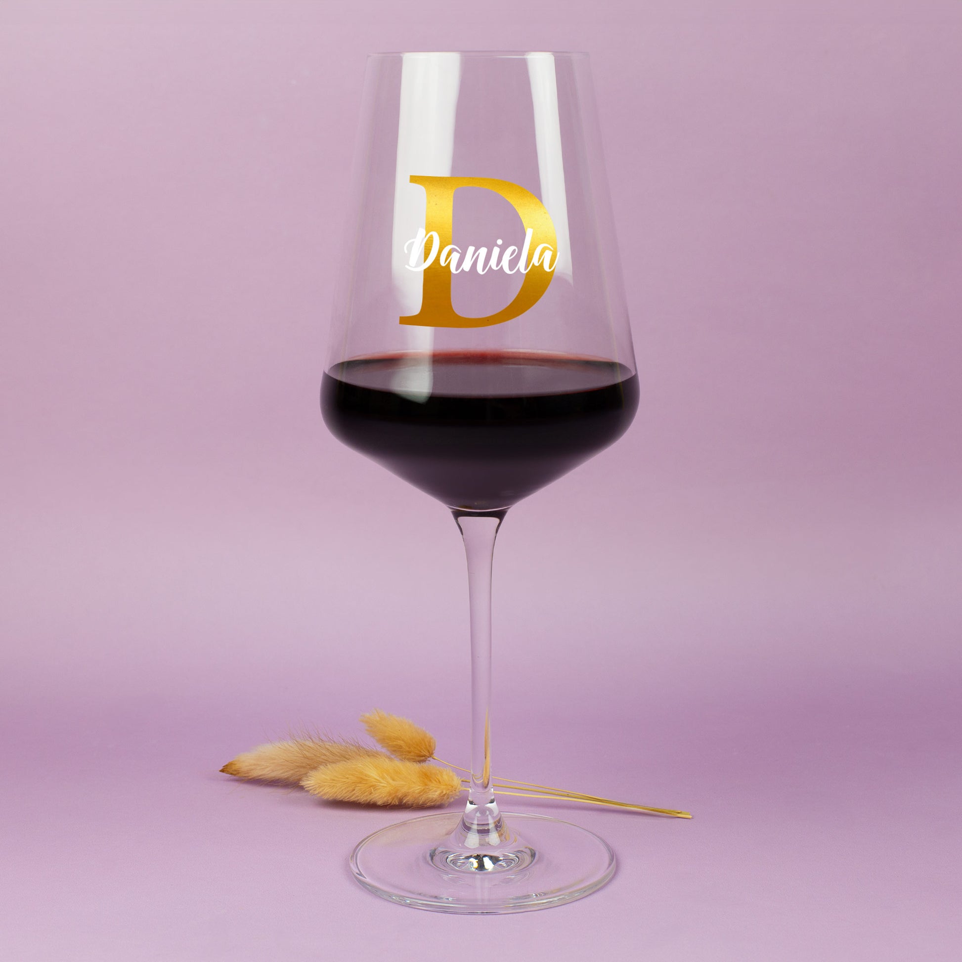 Personalisierbares Weinglas von Leonardo mit Initiale D und Name Daniela vor pastellfarbenem Hintergrund