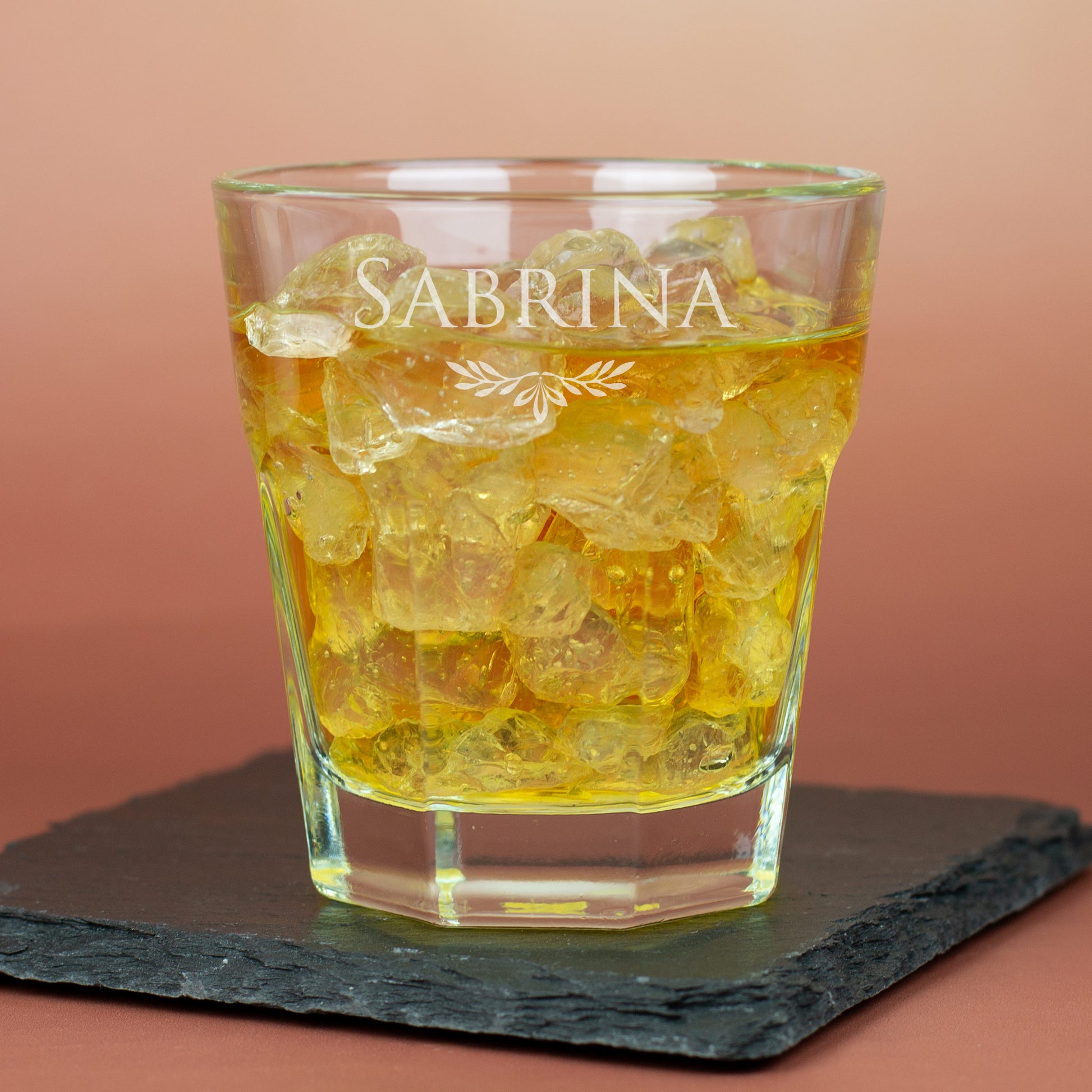 Leonardo-Trinkglas mit Gravur von Name und Ornament, gefüllt mit Eiswürfeln und Getränk auf Schieferplatte