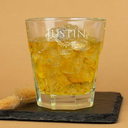 Leonardo-Trinkglas mit Gravur und Verzierung, goldfarbenes Getränk mit Eiswürfeln auf dunkler Schieferplatte