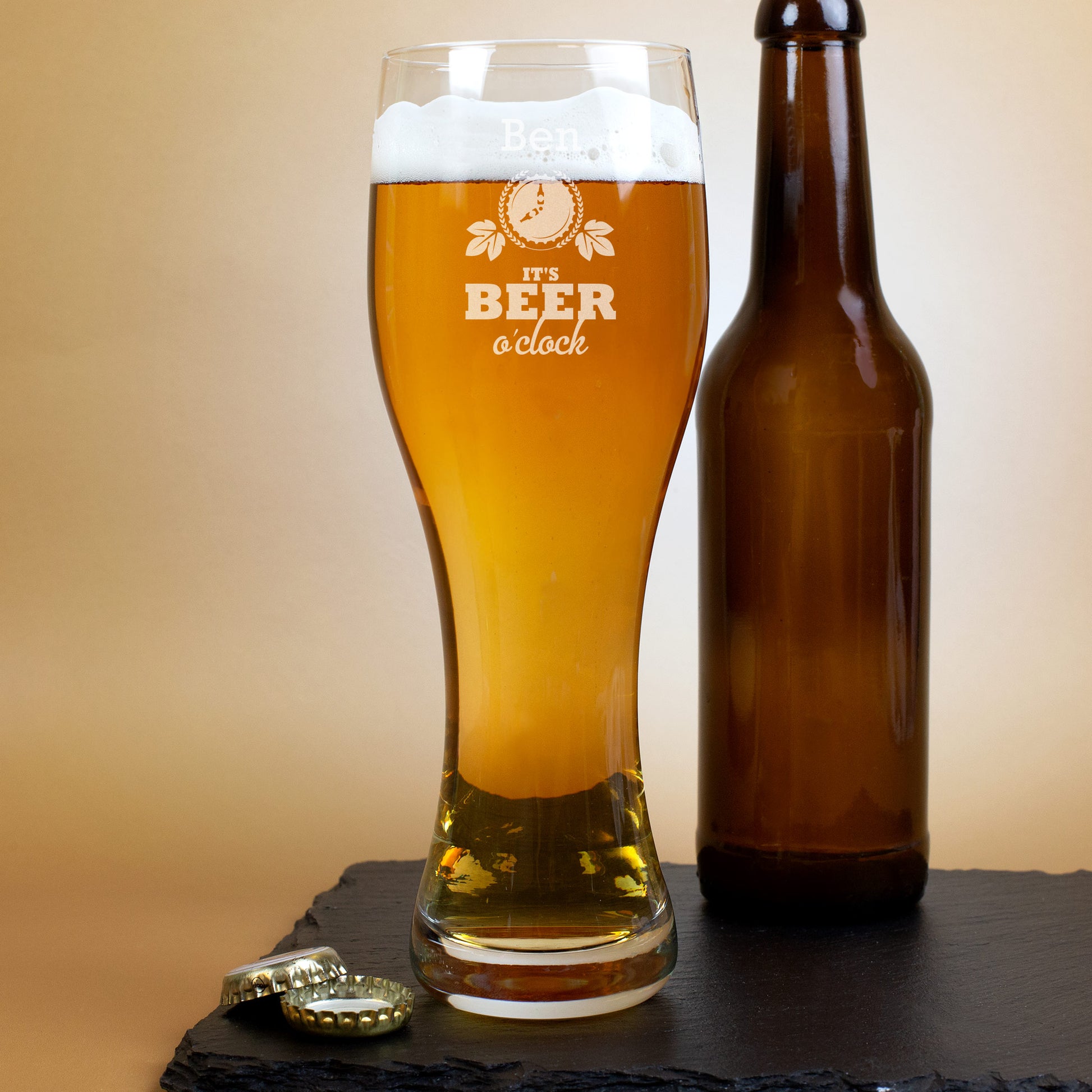 Personalisierbares Leonardo-Weizenglas mit Gravur „It’s Beer o’clock“, befüllt mit Bier und daneben braune Bierflasche