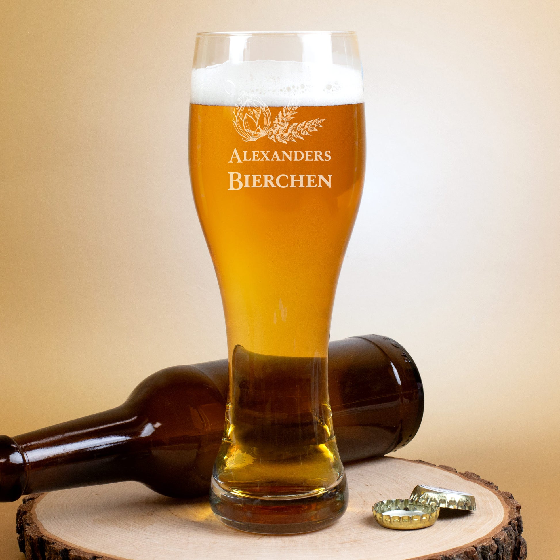 Personalisiertes Weizenglas mit Gravur „Alexanders Bierchen“, gefüllt mit Bier, daneben eine Flasche und Kronkorken