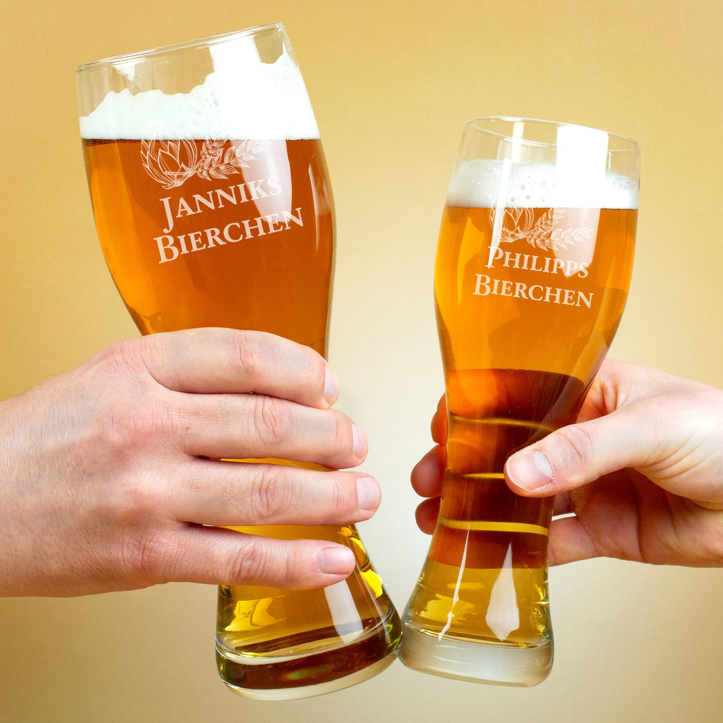 Zwei gravierte Weizengläser mit Bier, in Händen beim Anstoßen, Gravuren „Janniks Bierchen“ und „Philipps Bierchen“