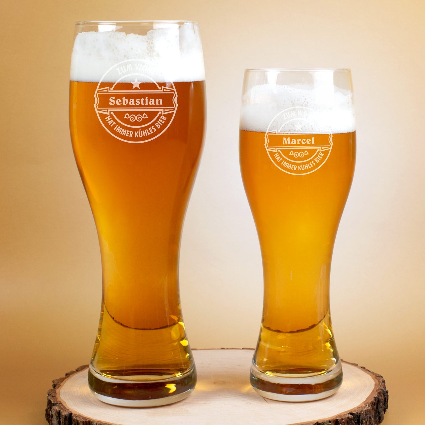 Zwei Weizengläser mit Gravur „Sebastian“ und „Marcel“ stehen nebeneinander auf einer Holzscheibe, unterschiedlich groß, beide mit Bier gefüllt.
