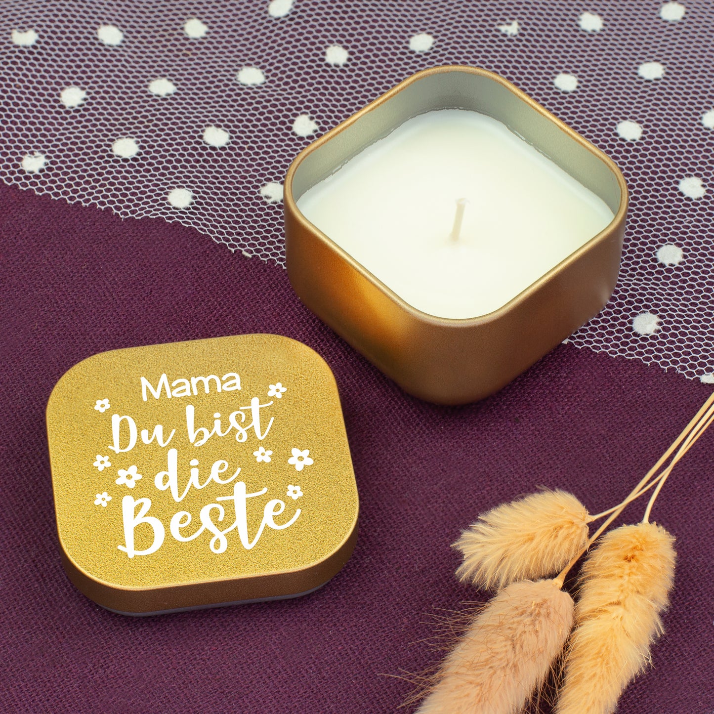 Geöffnete goldene Duftkerze mit Vanilleduft, Deckel mit Aufschrift „Mama Du bist die Beste“ auf violettem Stoff