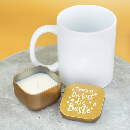 Goldene Duftkerze mit Vanilleduft neben weißer Tasse, Deckel mit Aufschrift „Tantchen Du bist die Beste“