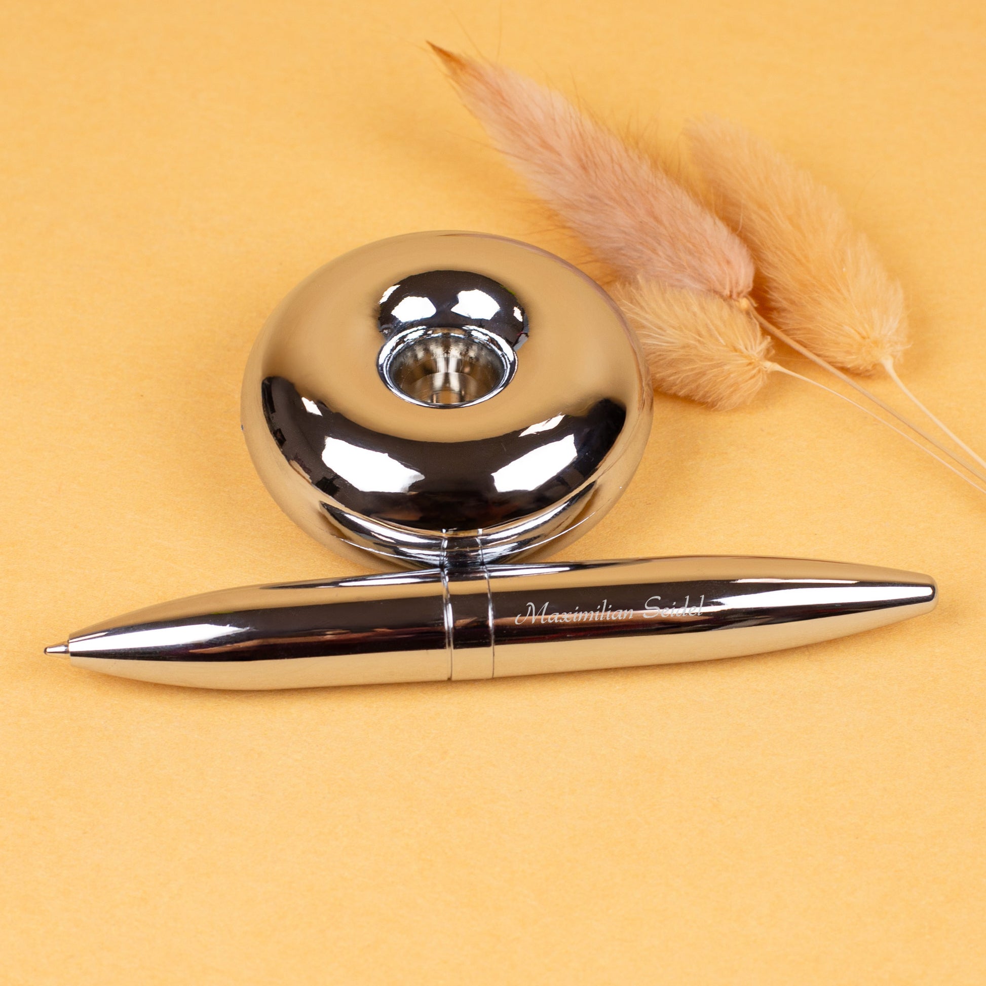 Magischer Kugelschreiber mit Namensgravur liegend neben Ständer auf gelbem Hintergrund