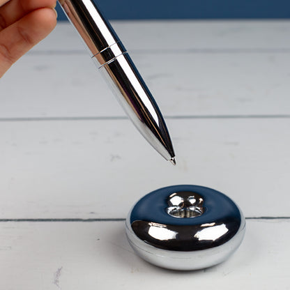 Magischer Kugelschreiber mit Namensgravur gehalten von einer Hand über Ständer