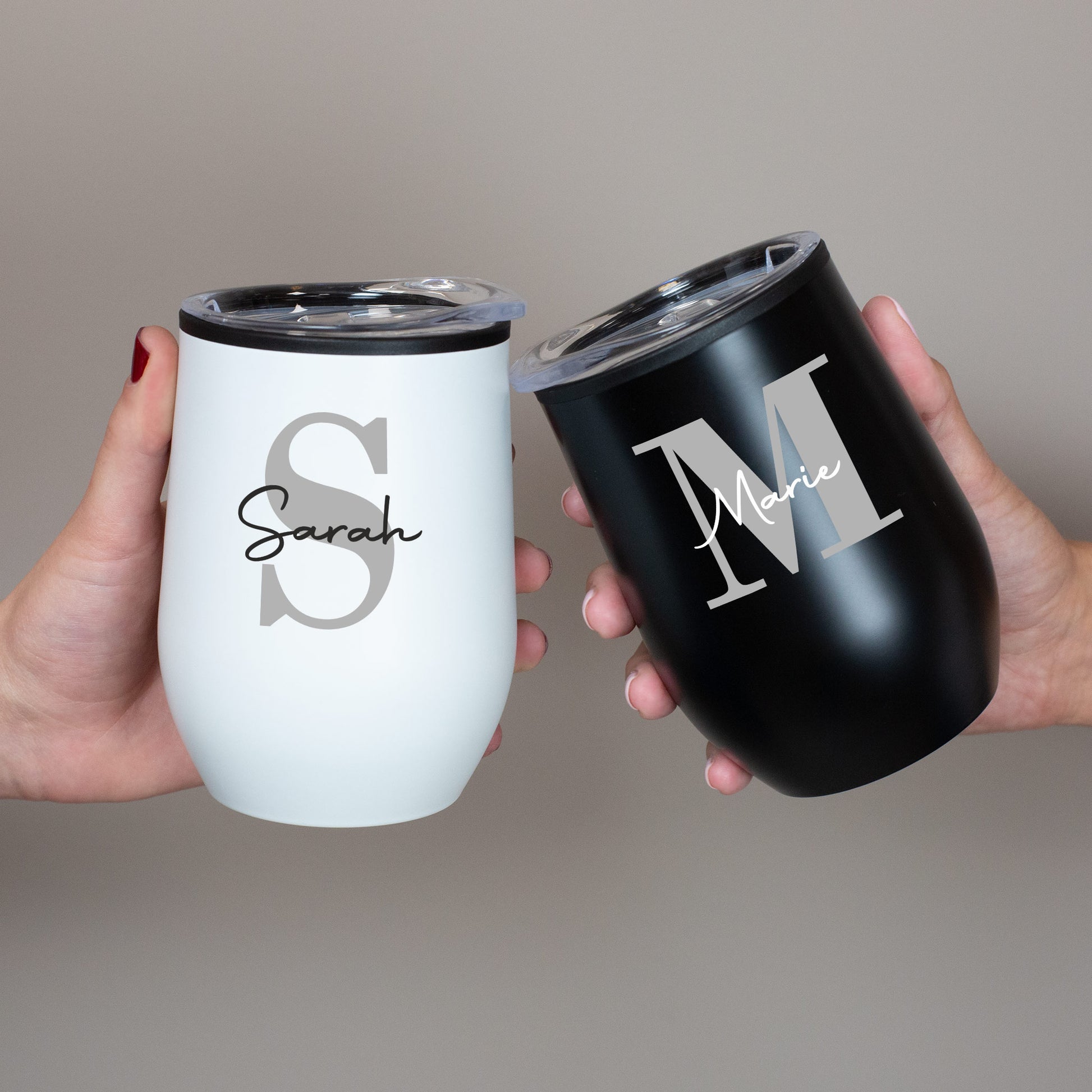 Zwei personalisierte Thermobecher in Weiß und Schwarz mit Initiale und Name, gehalten von zwei Händen