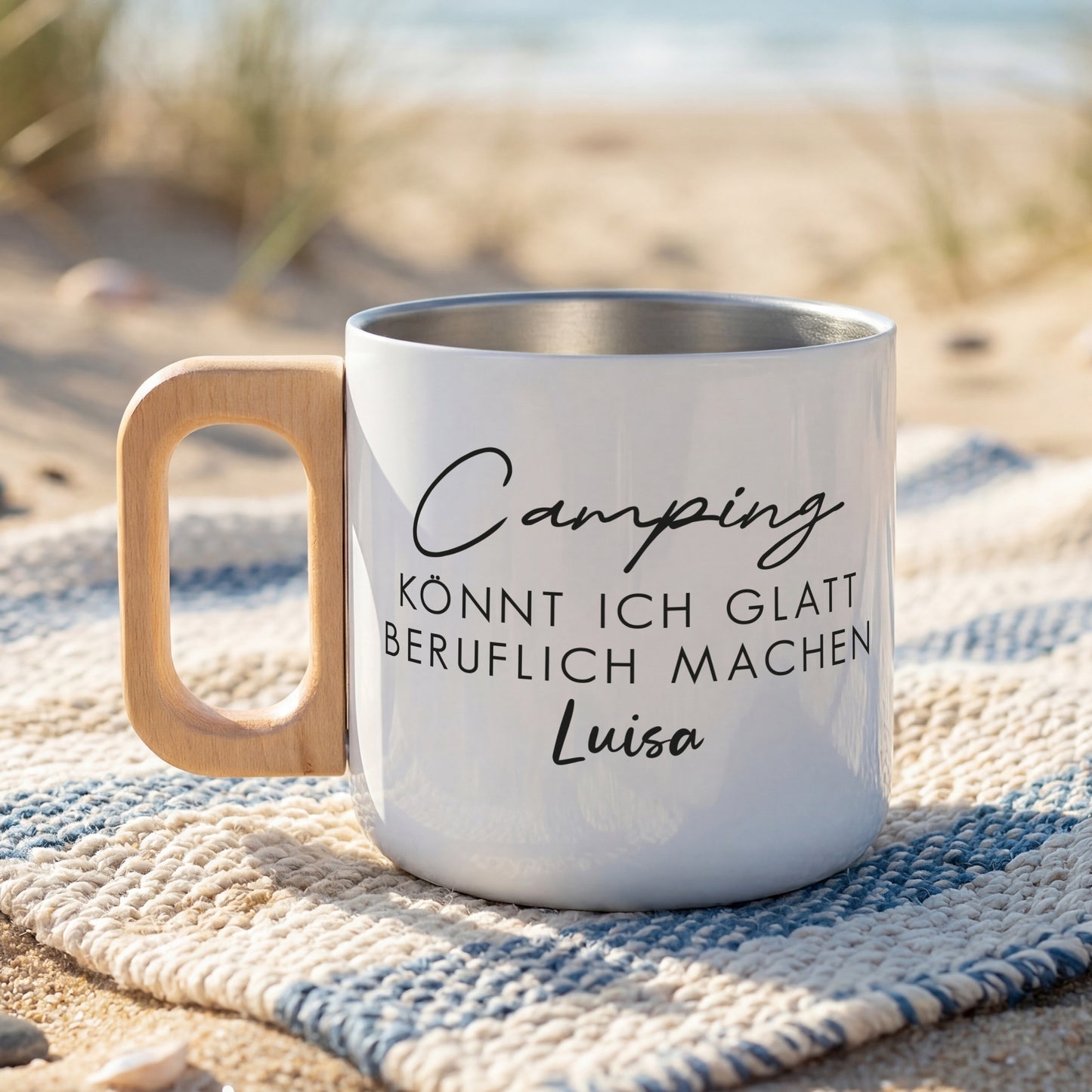 Weißer Edelstahlbecher am Strand mit Spruch „Camping könnt ich glatt beruflich machen“ und Name Luisa