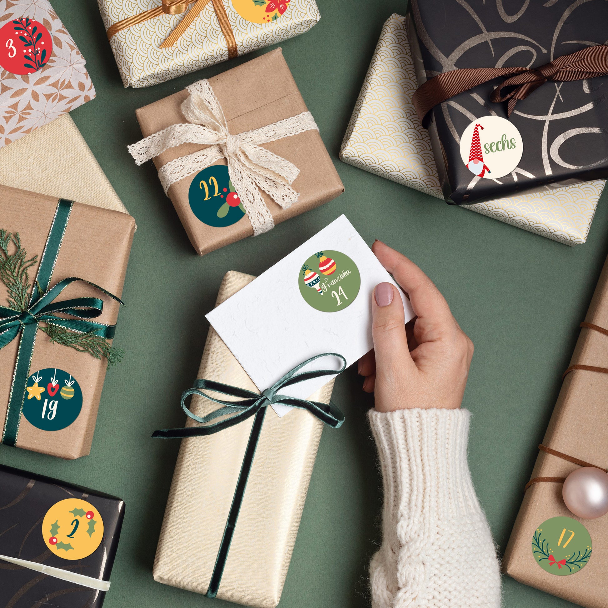Hand befestigt einen personalisierten Adventskalender-Aufkleber mit Weihnachtsmotiv auf ein Geschenk