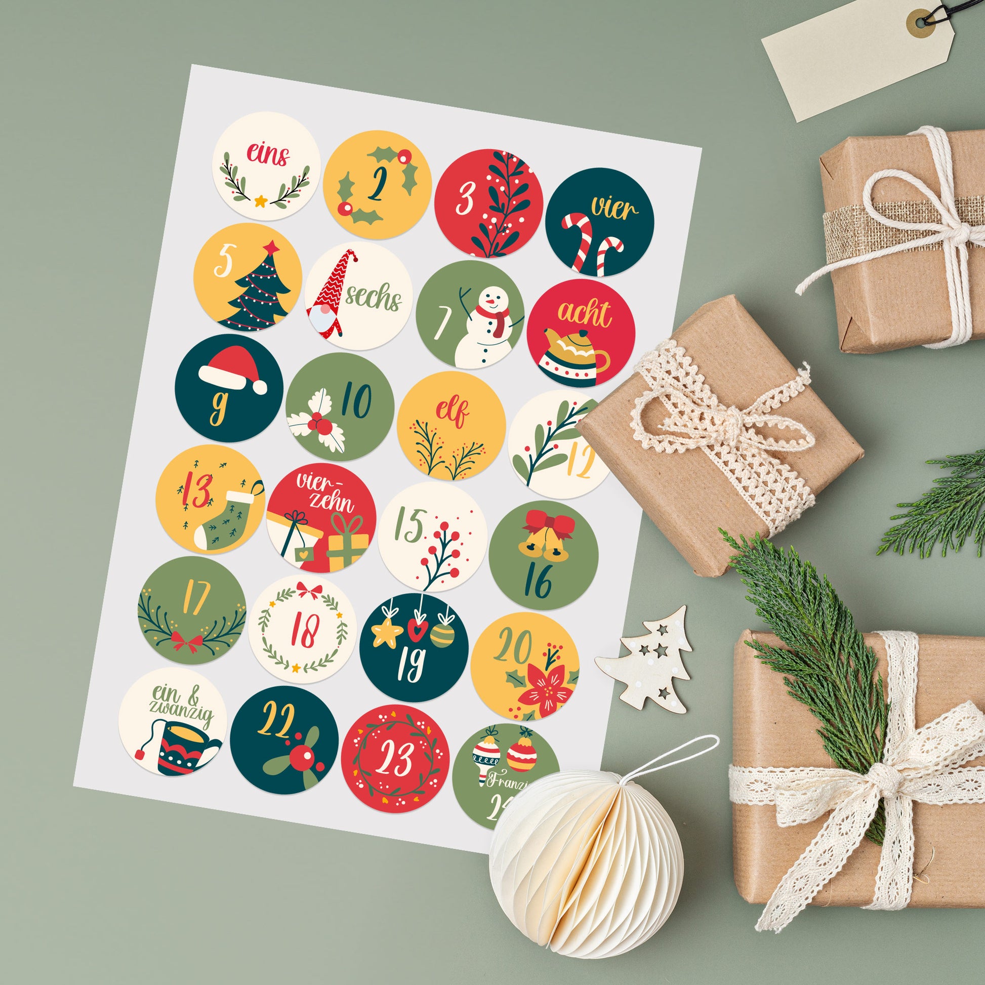 Bogen mit 24 bunten Adventskalender-Stickern mit Weihnachtsmotiven und Zahlen von 1–24 - daneben kleine Geschenke und Dekoration