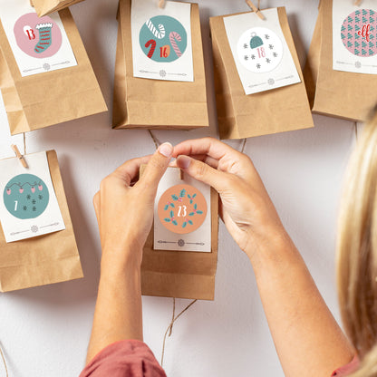 Hände kleben einen rosa Sticker mit der Zahl 13 an eine Adventskalender-Tüte