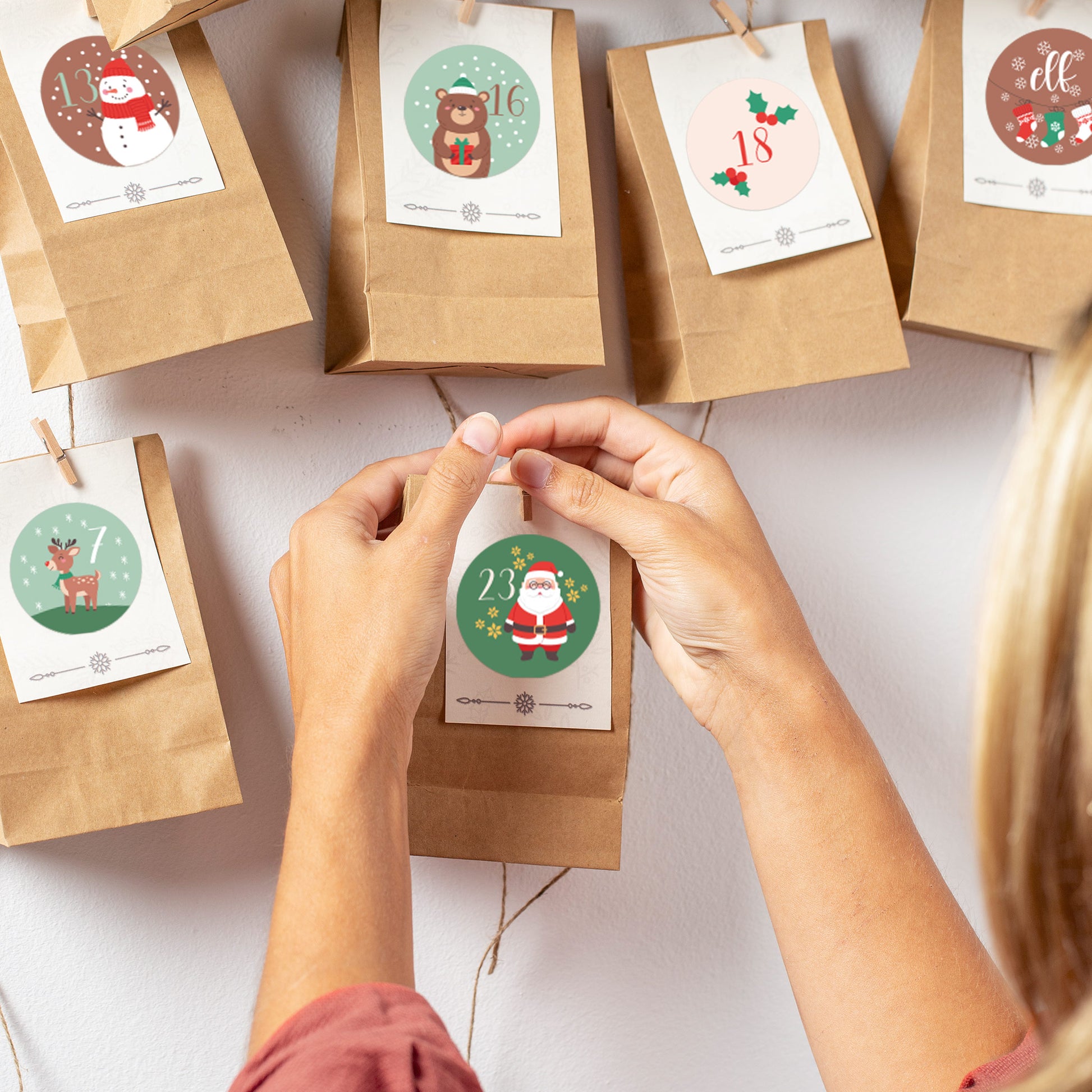 Detailaufnahme: Hände kleben Sticker mit Weihnachtsmann auf Papiertüte für DIY-Adventskalender