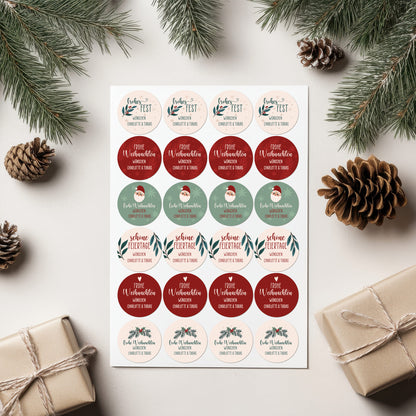 Geschenkverpackungen und Tannenzapfen dekorativ arrangiert mit Weihnachtsaufklebern „Frohes Fest“ und „Frohe Weihnachten“, personalisiert mit Namen.