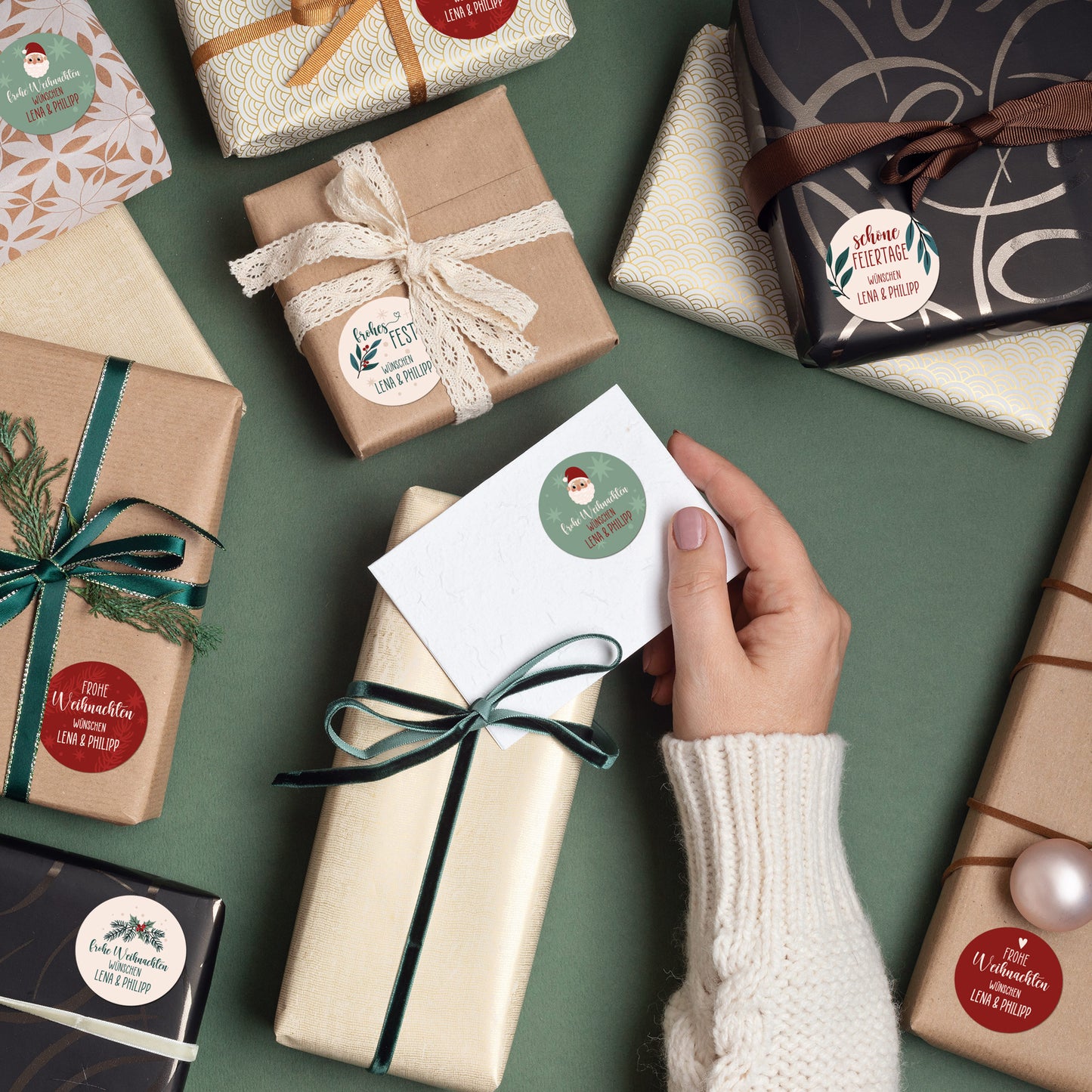 Verschiedene Geschenke und Karte mit runden Aufklebern, personalisiert mit Namen und Weihnachtsmotiven wie Weihnachtsmann und Mistelzweigen.