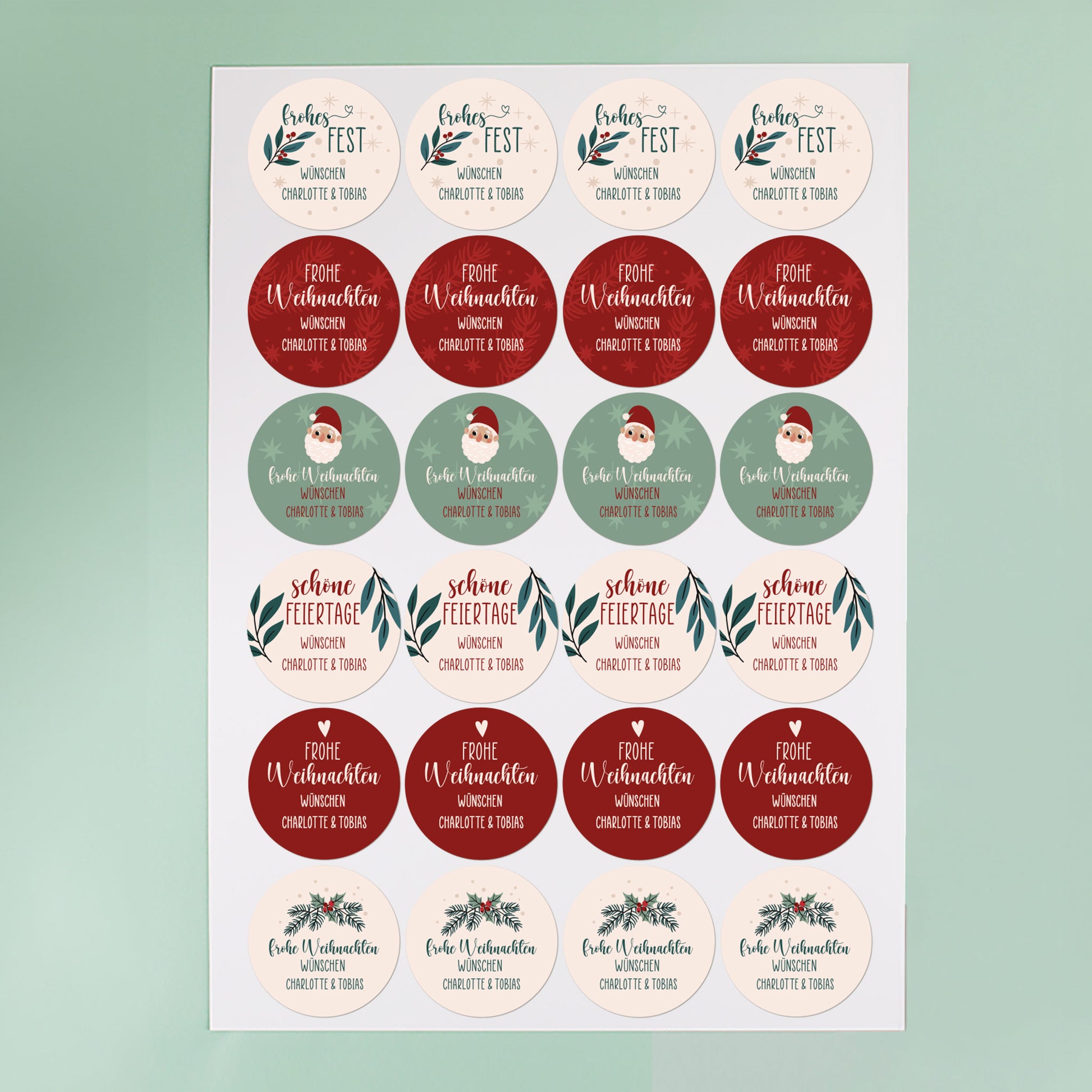 Bogen mit 24 runden Weihnachtsaufklebern in Rot, Grün und Beige, personalisierbar mit Text, vor mintgrünem Hintergrund fotografiert.