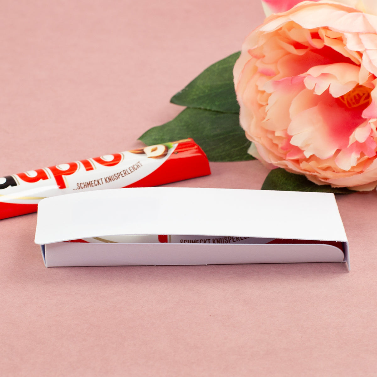 Geöffnete Geschenkverpackung für duplo Riegel mit Schokolade und Blume auf rosa Hintergrund
