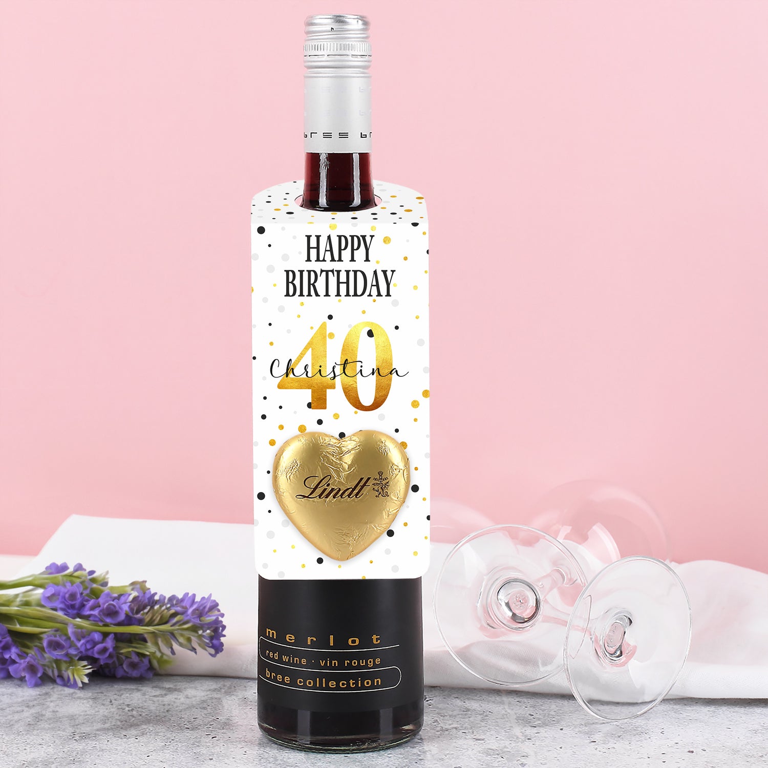 Großer Flaschenanhänger zum Geburtstag mit Konfetti-Motiv, personalisiertem Namen und Alter sowie goldenem Lindt-Herz – auf einer Flasche platziert.