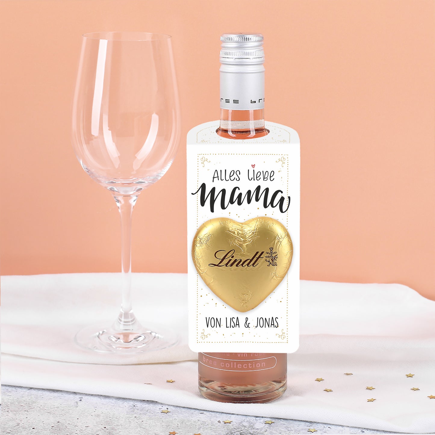 Nahaufnahme des aufgeklebt goldenen Lindt Schokoladenherzens auf dem kleinen weißen Flaschenanhänger.