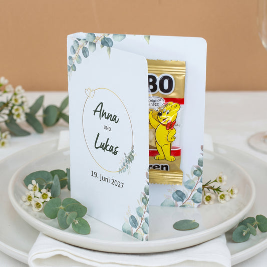Geöffnetes Hochzeits-Gastgeschenk mit Namen des Paares und Haribo Goldbären im Klappkärtchen