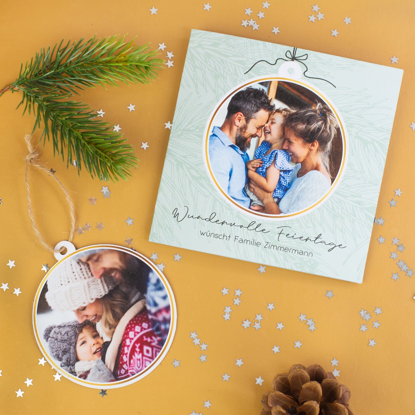 Quadratische Weihnachtskarte mit herausnehmbarer runder Fotokugel und zweitem Foto, dekoriert mit Tannenzweig, Sternkonfetti und Tannenzapfen auf goldenem Hintergrund