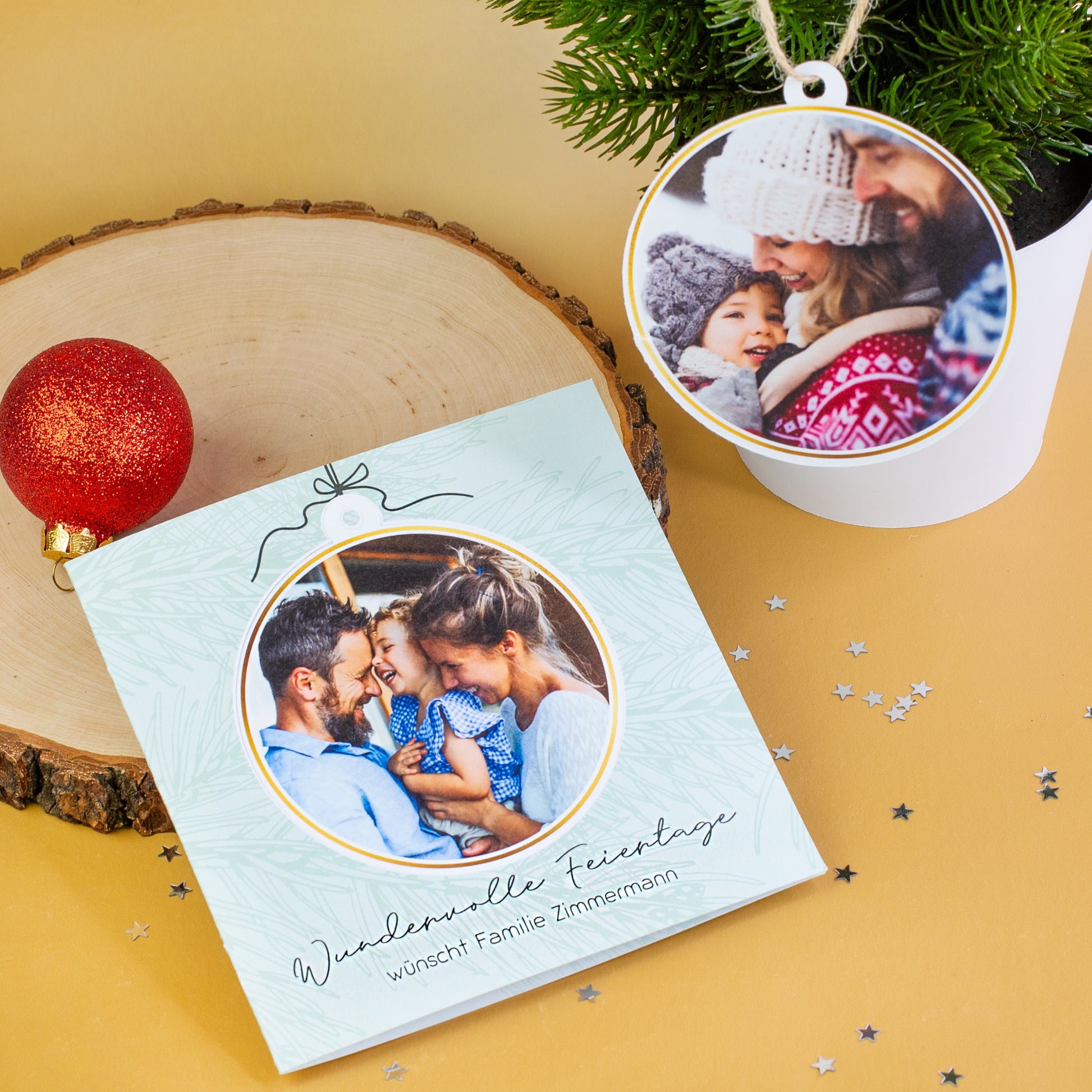 Weihnachtskarte mit Fotokugel, liegend auf Holzscheibe neben roter Kugel, zweite Fotokugel am kleinen Tannenbaum hängend