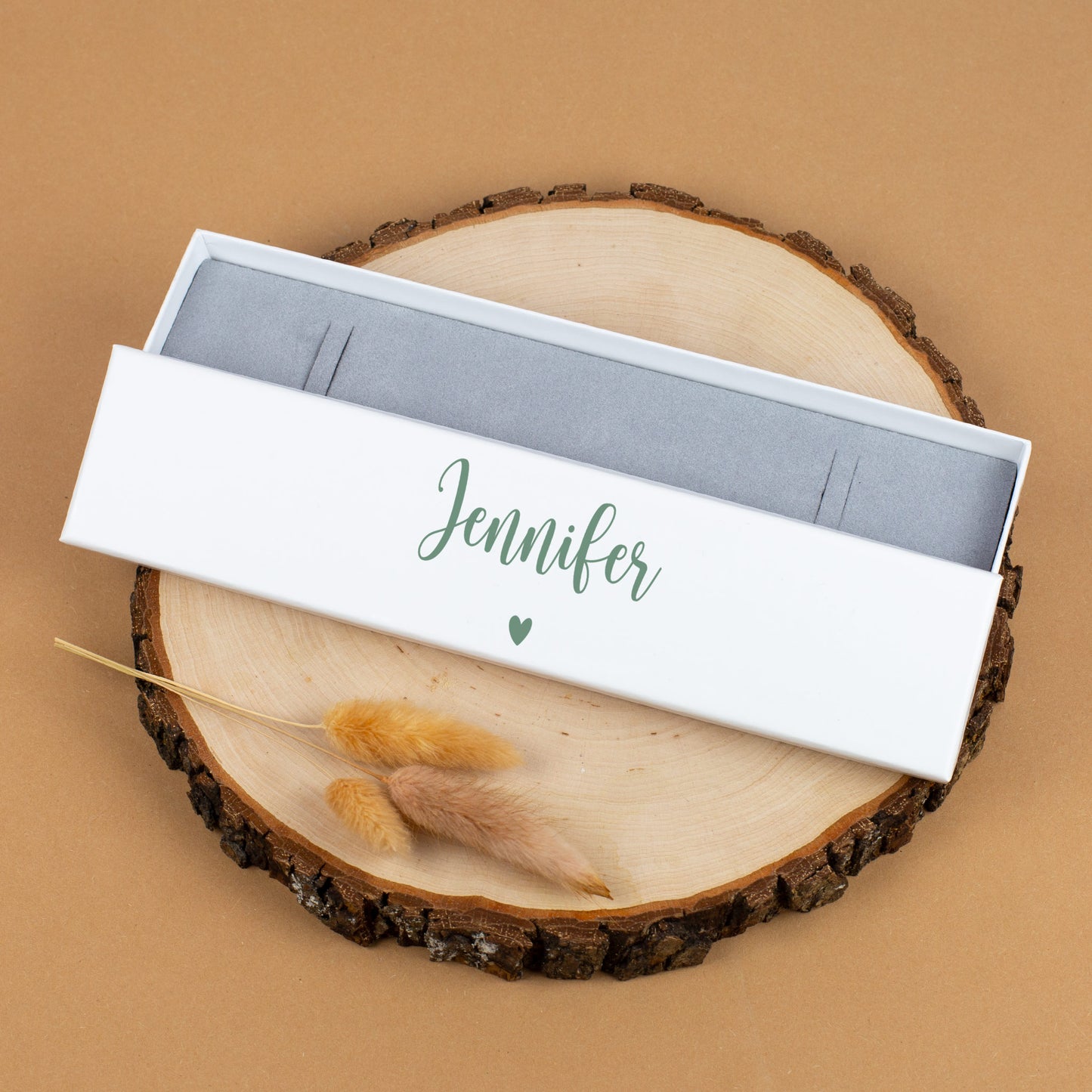 Geschenkbox in Weiß mit Name „Jennifer“ in Grün, dekorativ auf Holzscheibe
