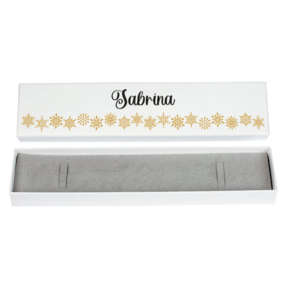 Freigestellte Schmuckverpackung aus weißem Karton mit goldenen Schneeflocken und dem Namen „Sabrina“. Der Deckel ist geöffnet und zeigt den grauen Innenschaum mit Armbandaussparungen. Studioaufnahme auf weißem Hintergrund.