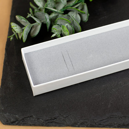 Detailaufnahme der geöffneten Schmuckbox mit grauem Schaumstoffeinsatz, liegend auf einer schwarzen Schieferplatte. Zweige mit Eukalyptusblättern dienen als Dekoration.