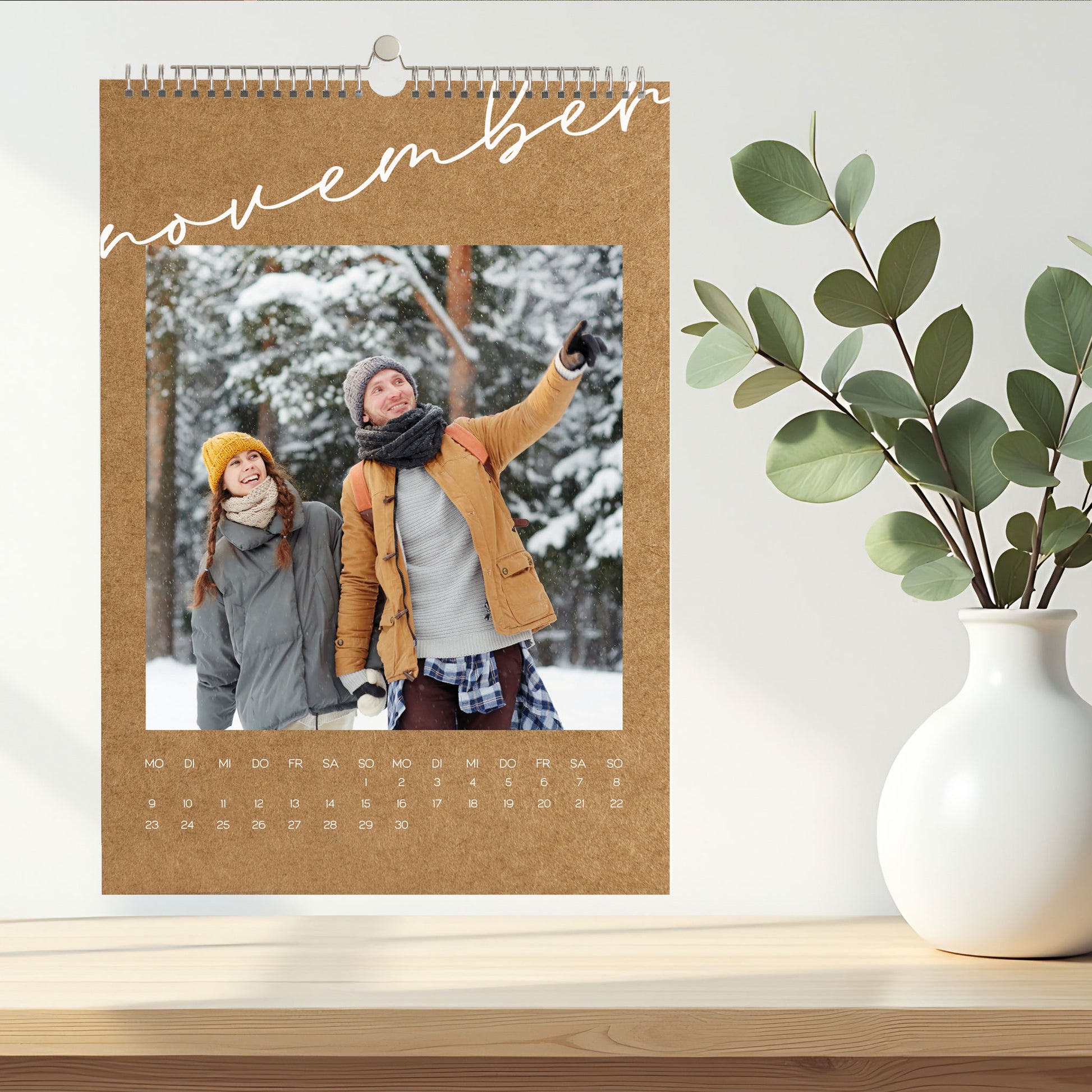 Foto-Wandkalender für November in natürlicher Kraftpapier-Optik, mit Winterfoto eines Paares im Schnee, dekoriert auf einem hellen Sideboard.