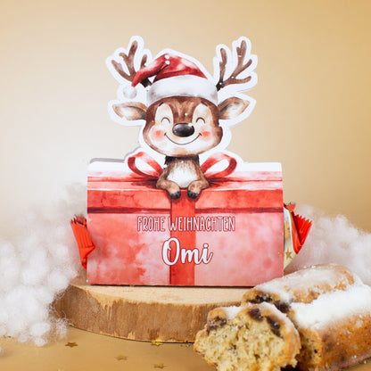 Rentier-Mini-Stollen mit personalisierter Verpackung – Aufdruck „Frohe Weihnachten Omi“, dekorativ auf Holzscheibe mit Stollenstücken und Kunstschnee.