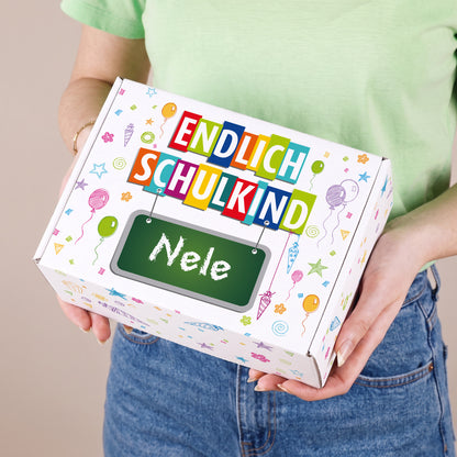 Kleine Geschenkbox zur Einschulung mit Wunschname und buntem Schulmotiv, in den Händen einer Person