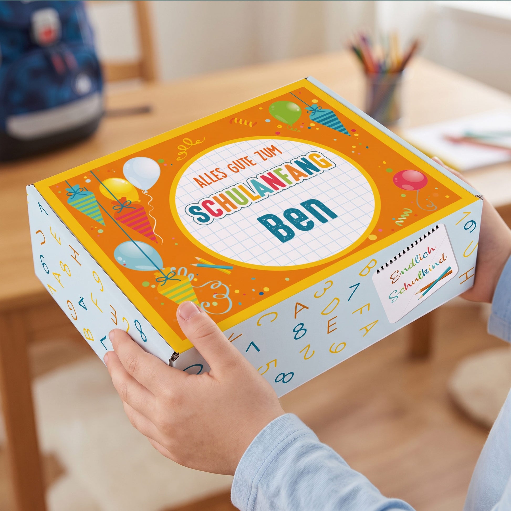 Kleine personalisierte Aufbewahrungsbox aus Pappe mit Name und buntem Schulanfang-Motiv in Kinderhänden
