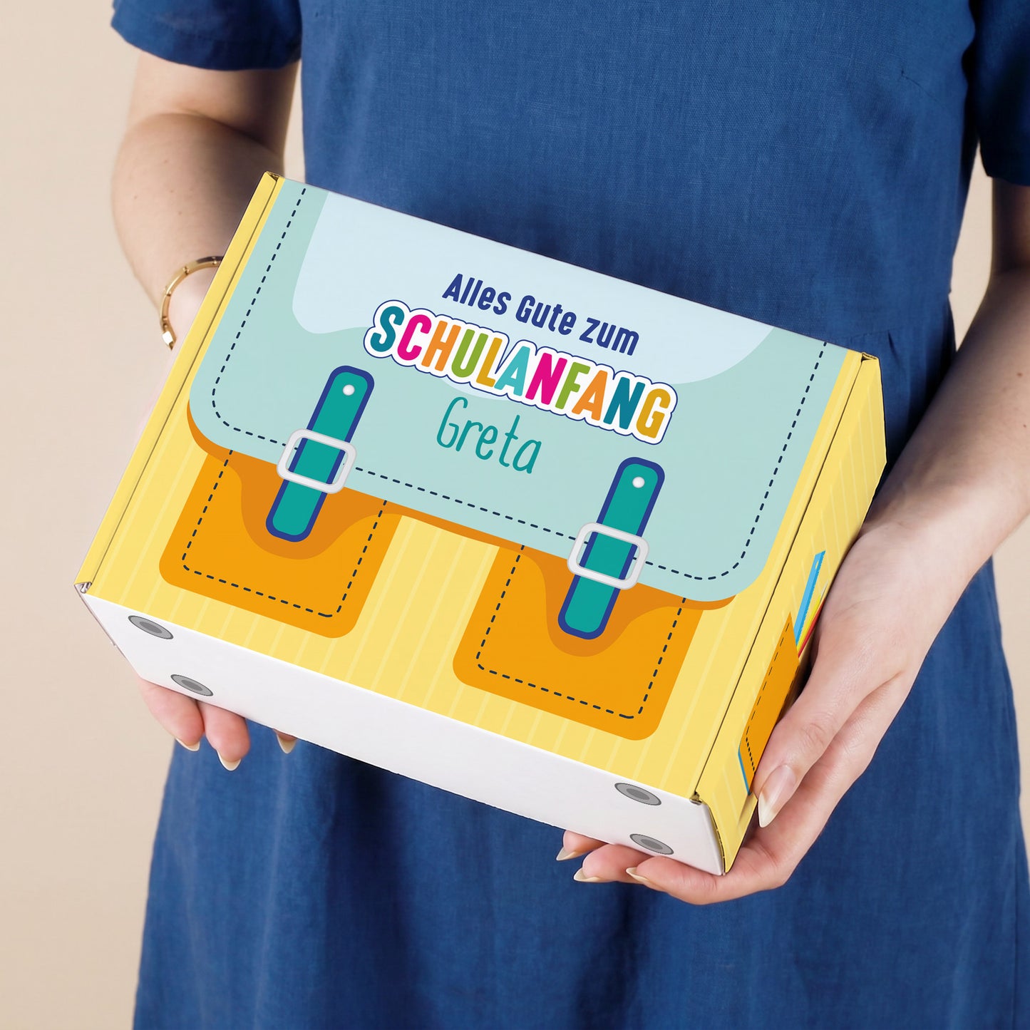 Kleine gelbe Geschenkbox zum Schulanfang mit Wunschname und Schulranzen Motiv, von einer Person gehalten