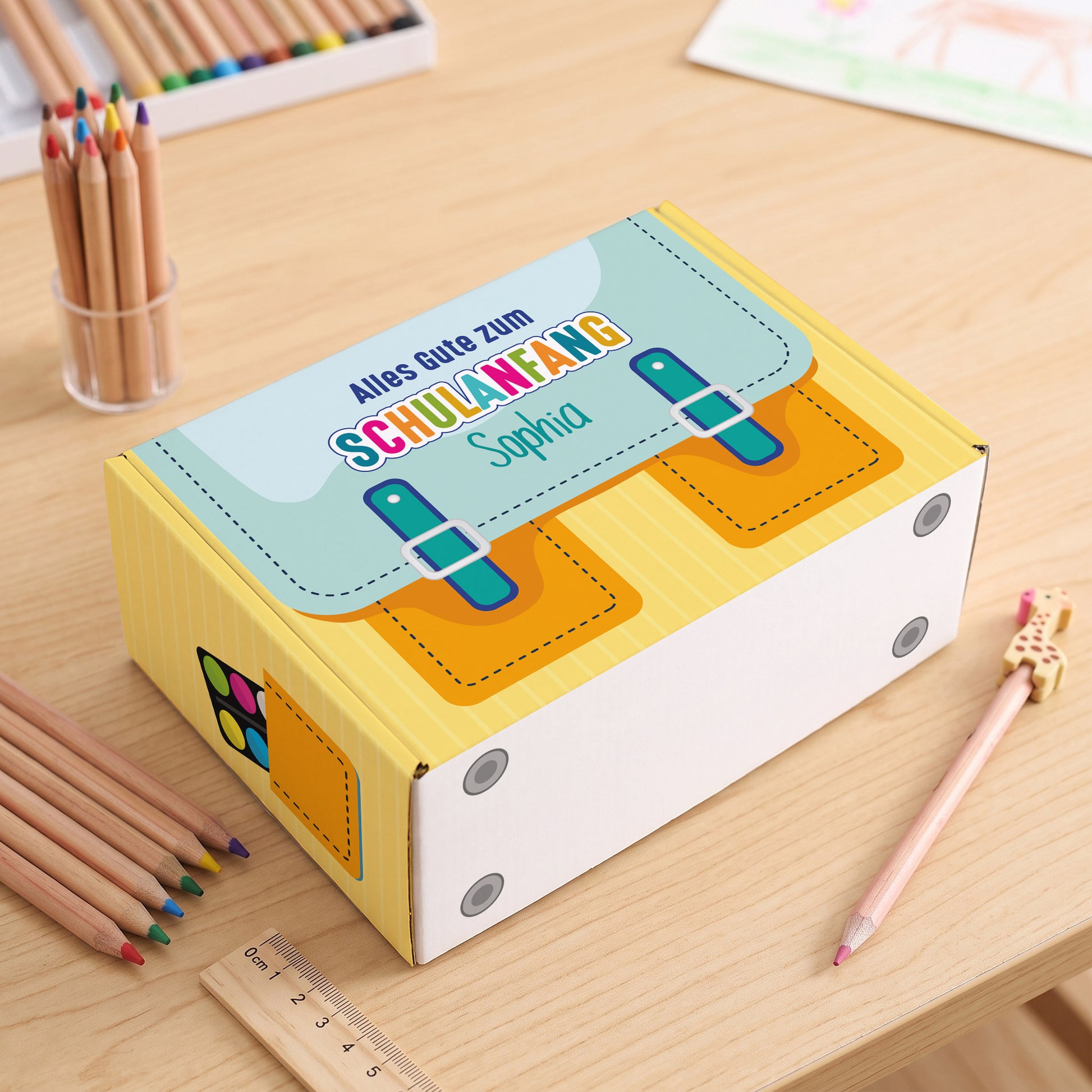 Kleine gelbe Pappbox zur Einschulung mit Name auf einem Schreibtisch liegend