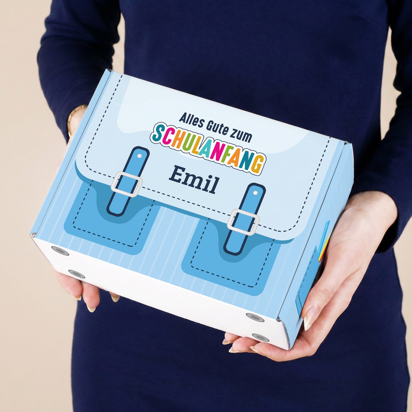 Kleiner personalisierter Geschenkkarton zur Einschulung in Blau mit Schulranzen-Motiv und Name, von einer Person gehalten