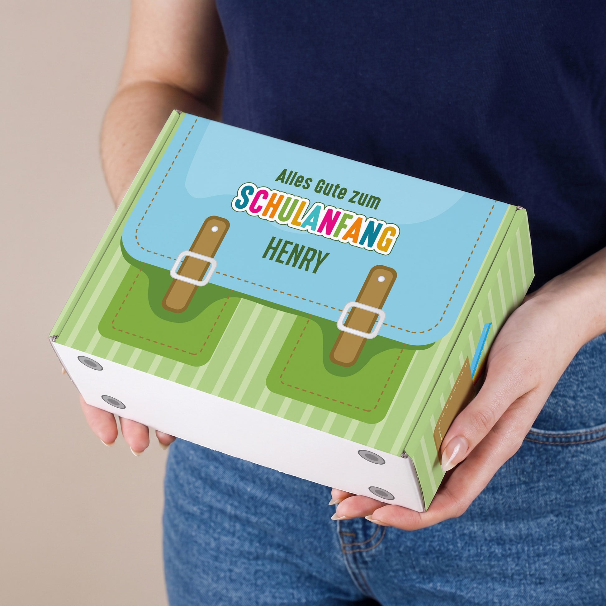 Kleine grüne Geschenkbox mit Name und Schulranzen-Motiv zum Schulanfang wird von einer Person gehalten