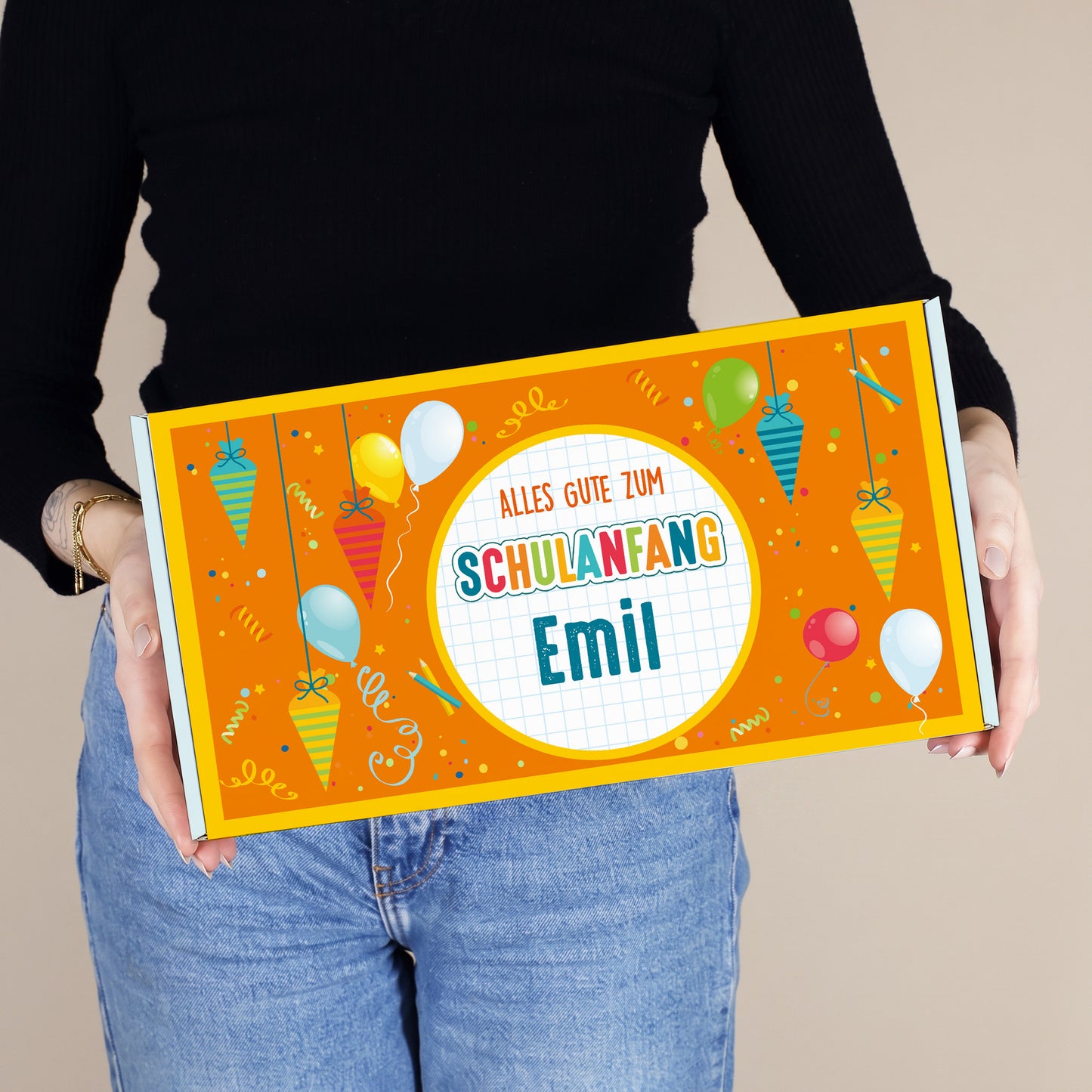 Mittlere personalisierte Aufbewahrungsbox aus Pappe mit Wunschname und buntem Schulanfang-Motiv, von einer Person gehalten