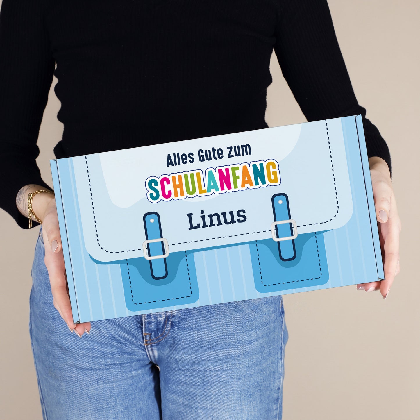 Mittlere blaue Geschenkverpackung zur Einschulung mit Name, von einer Person gehalten