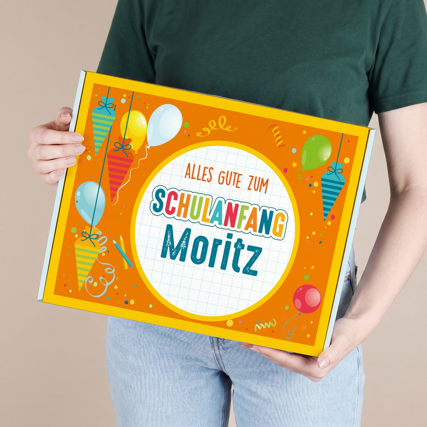 Große personalisierte Pappbox mit Name und buntem Motiv aus Schultüten und Luftballons, von einer Person gehalten