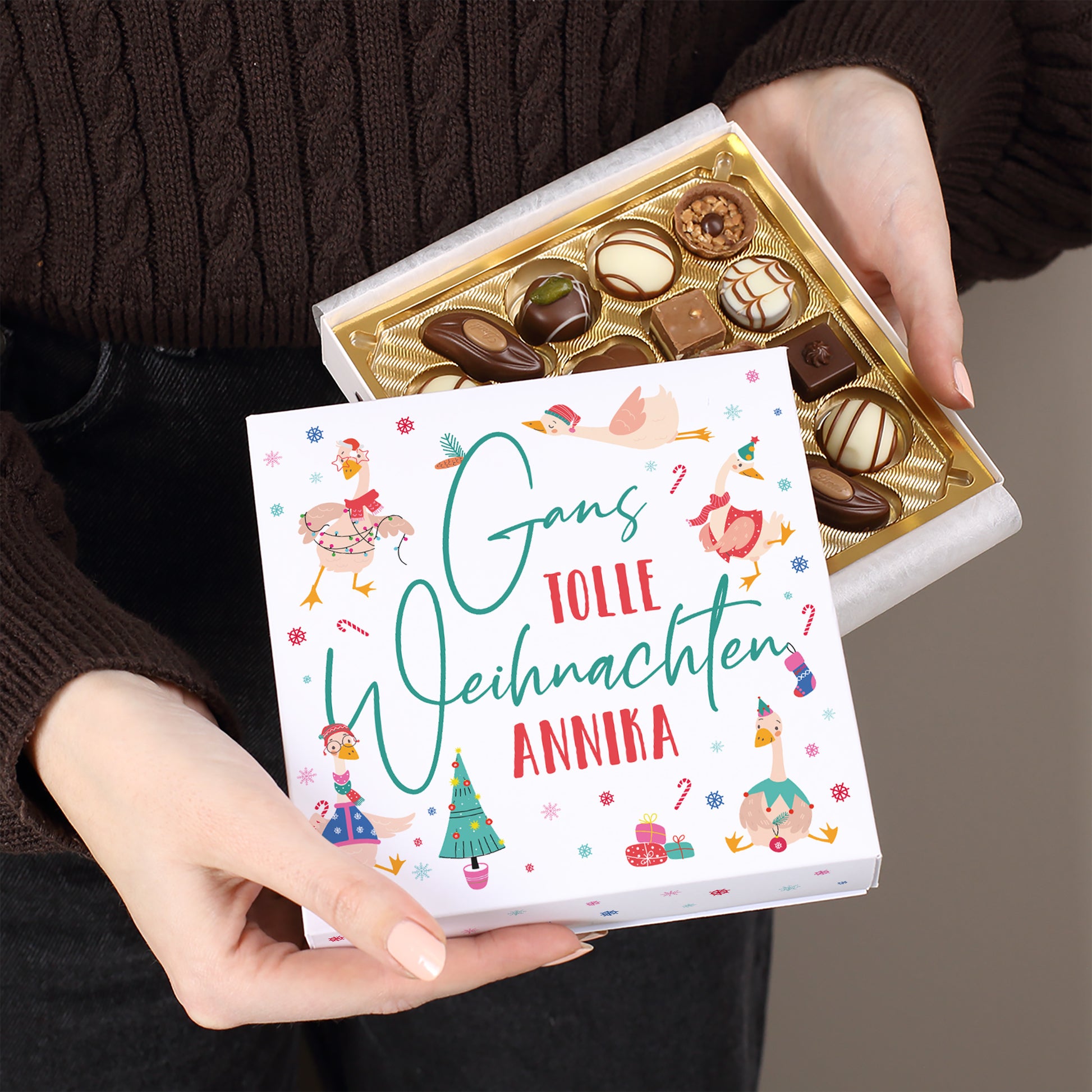 Geöffnete Lindt Pralinenverpackung mit Spruch „Gans tolle Weihnachten Annika“, gehalten in beiden Händen, goldene Einlage mit Schokolade sichtbar.