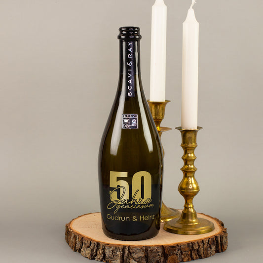 Personalisierte Prosecco-Flasche zur goldenen Hochzeit mit Gravur 50 Jahre gemeinsam neben weißen Kerzen