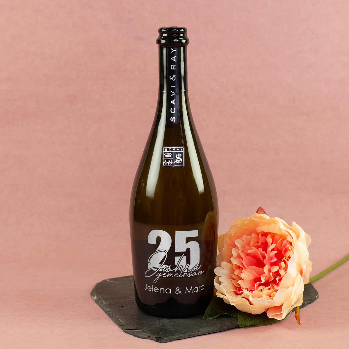 Personalisierte Scavi & Ray Prosecco-Flasche zur Silberhochzeit mit Namen Jelena & Marc neben dekorativer Blume