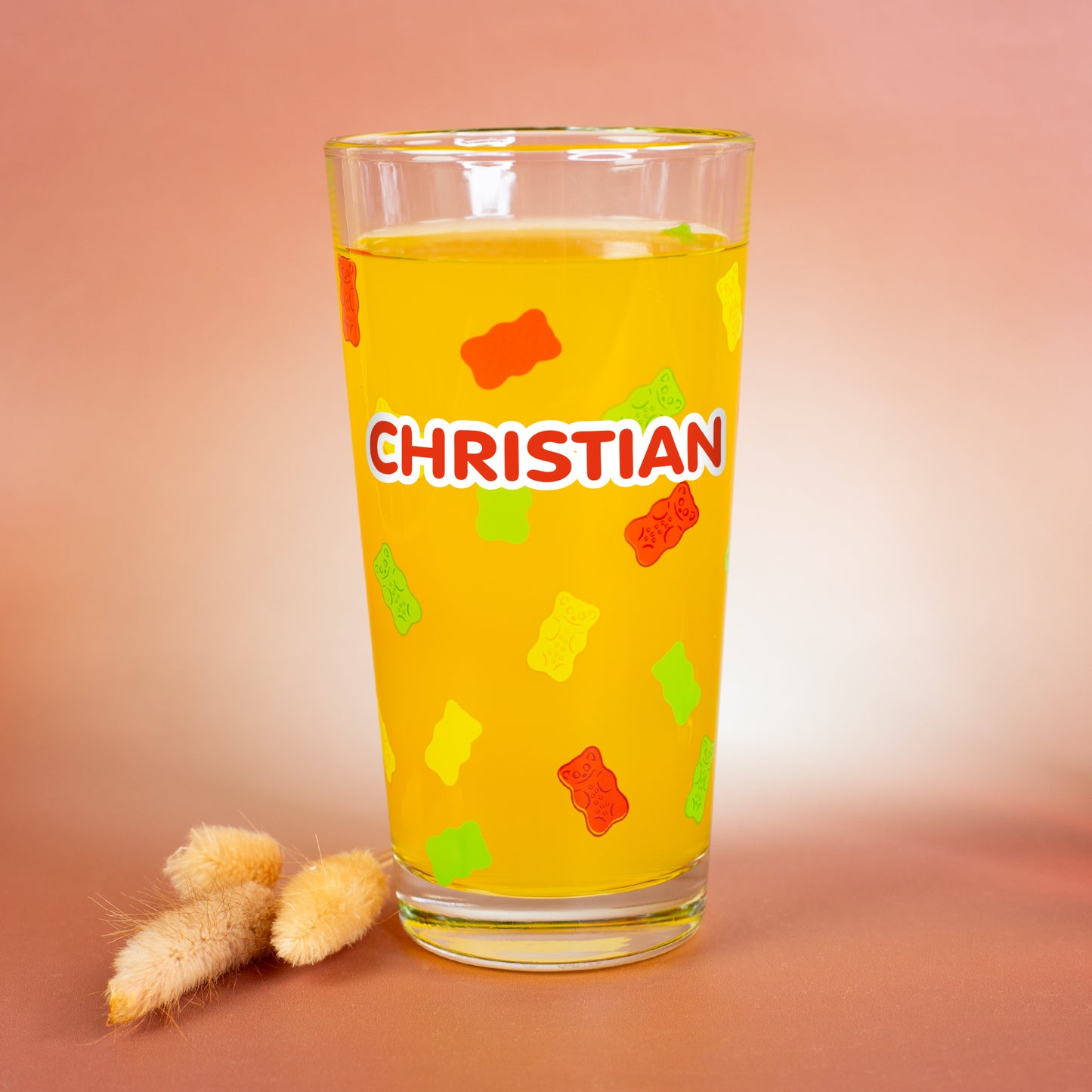 HARIBO Trinkglas mit personalisiertem Namen „Christian“, bunt bedruckte Gummibärchen rundum, dekoriert mit Trockenblumen auf warmem Hintergrund.