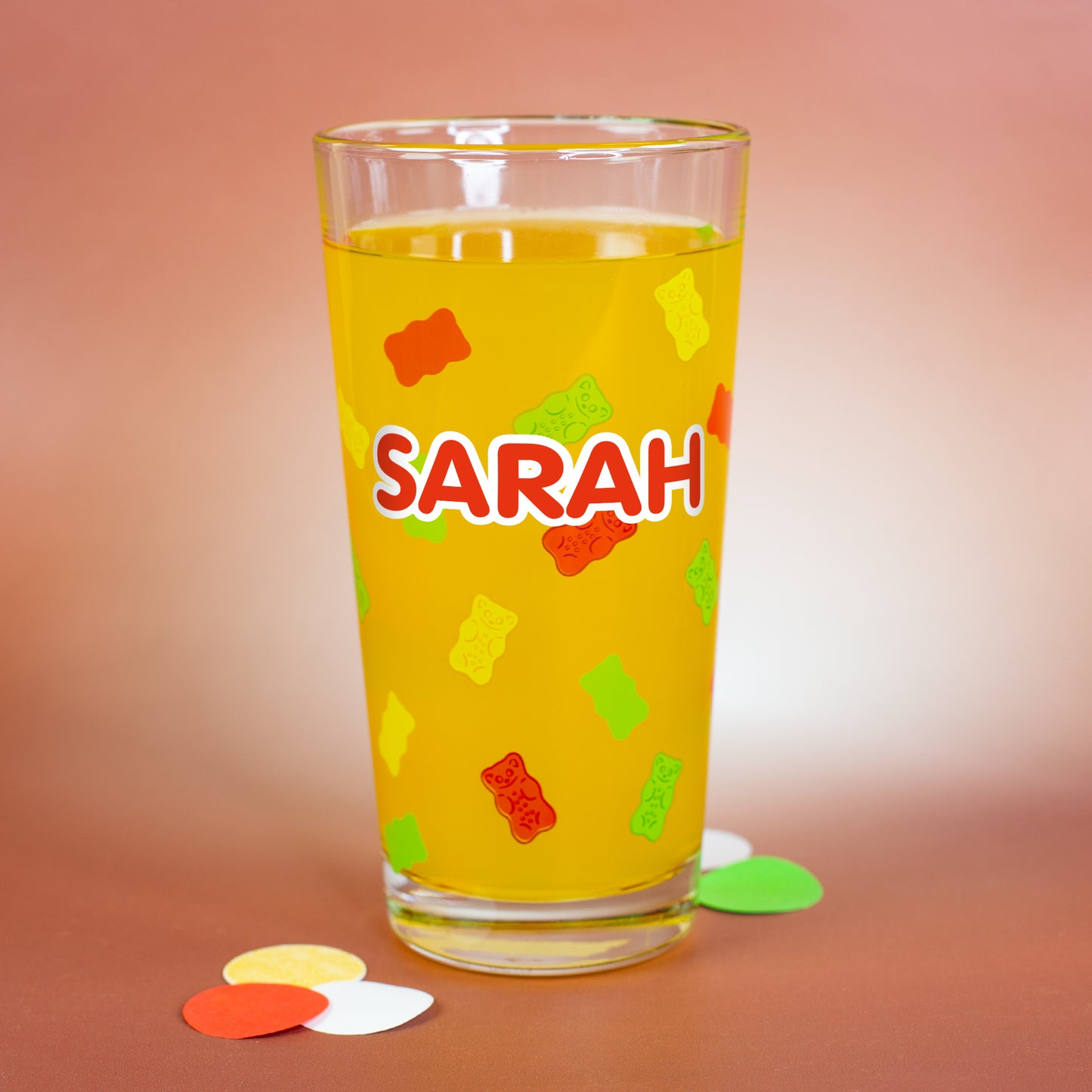Personalisierbares HARIBO Glas mit bunten Gummibärchenmotiven und großem weißen Namensdruck „Sarah“, gefüllt mit gelber Flüssigkeit.
