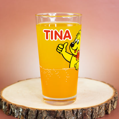 HARIBO Trinkglas mit Goldbär und orangem Unterbereich, personalisiert mit „Tina“, auf Holzscheibe.