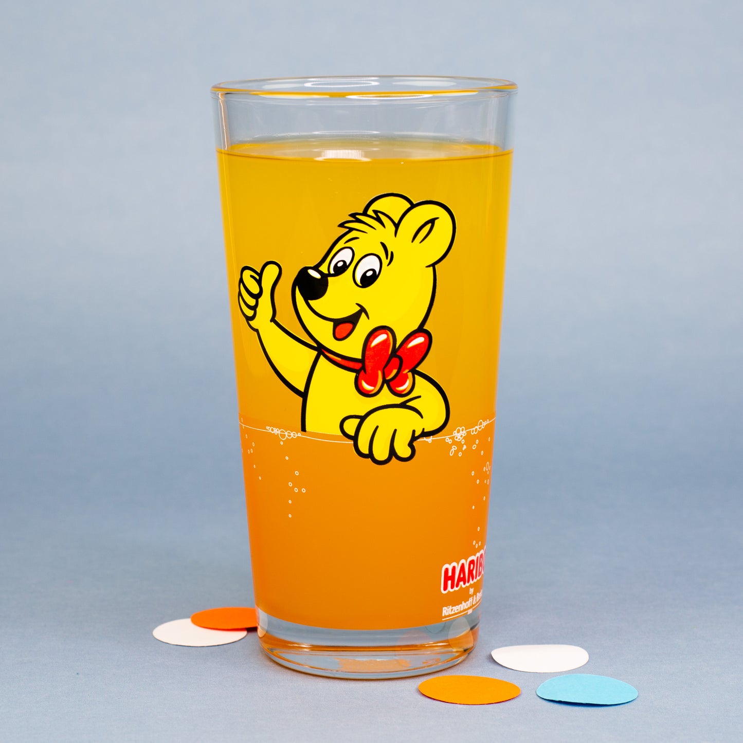 HARIBO Trinkglas in Orange mit Goldbär Motiv und orangefarbenem Getränk auf grauem Hintergrund
