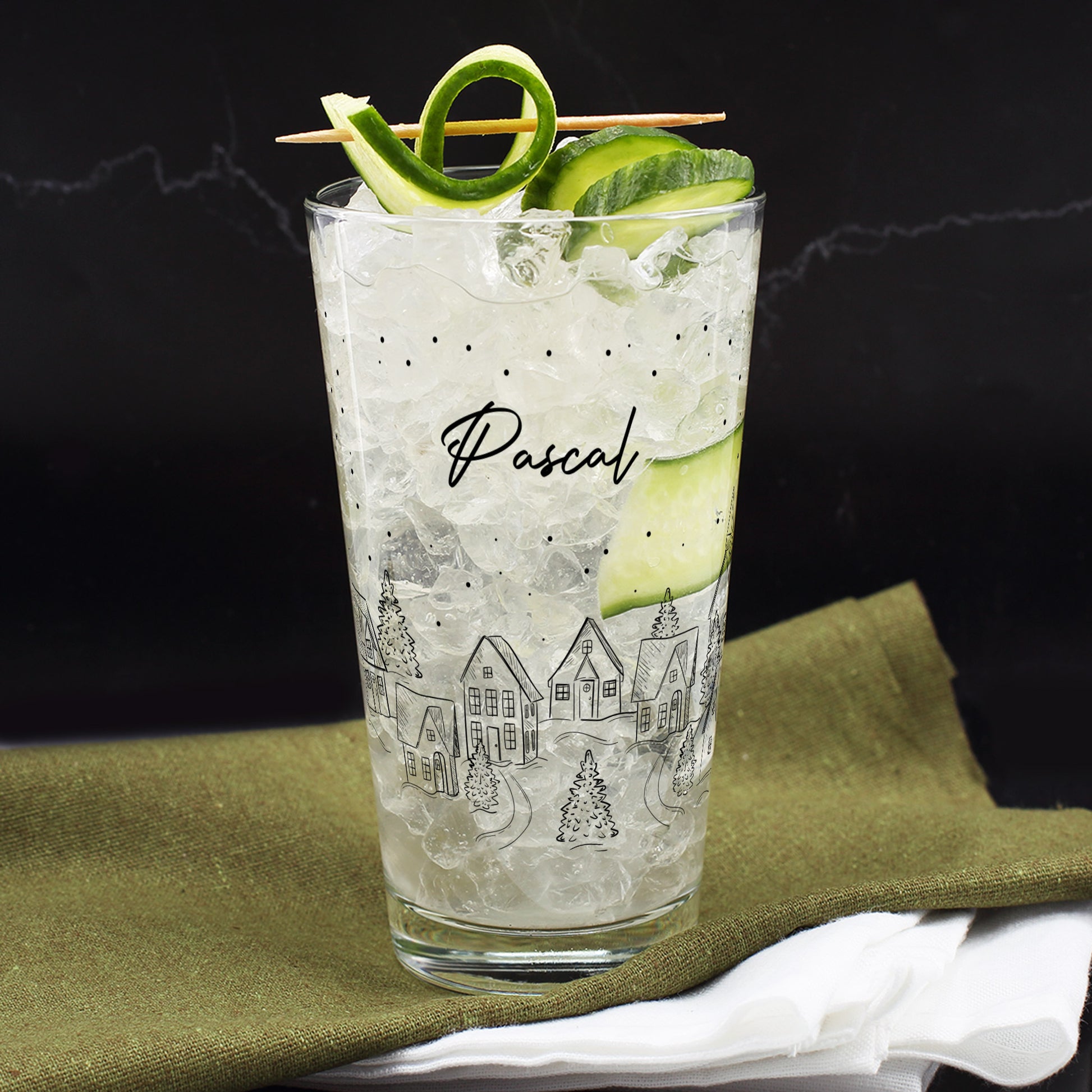 Winterliches Trinkglas mit festlichem Stadtdesign und Name Pascal, gefüllt mit Getränk und Gurken-Deko.