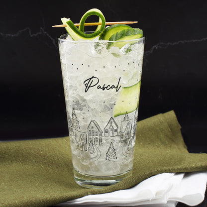 Winterliches Trinkglas mit festlichem Stadtdesign und Name Pascal, gefüllt mit Getränk und Gurken-Deko.